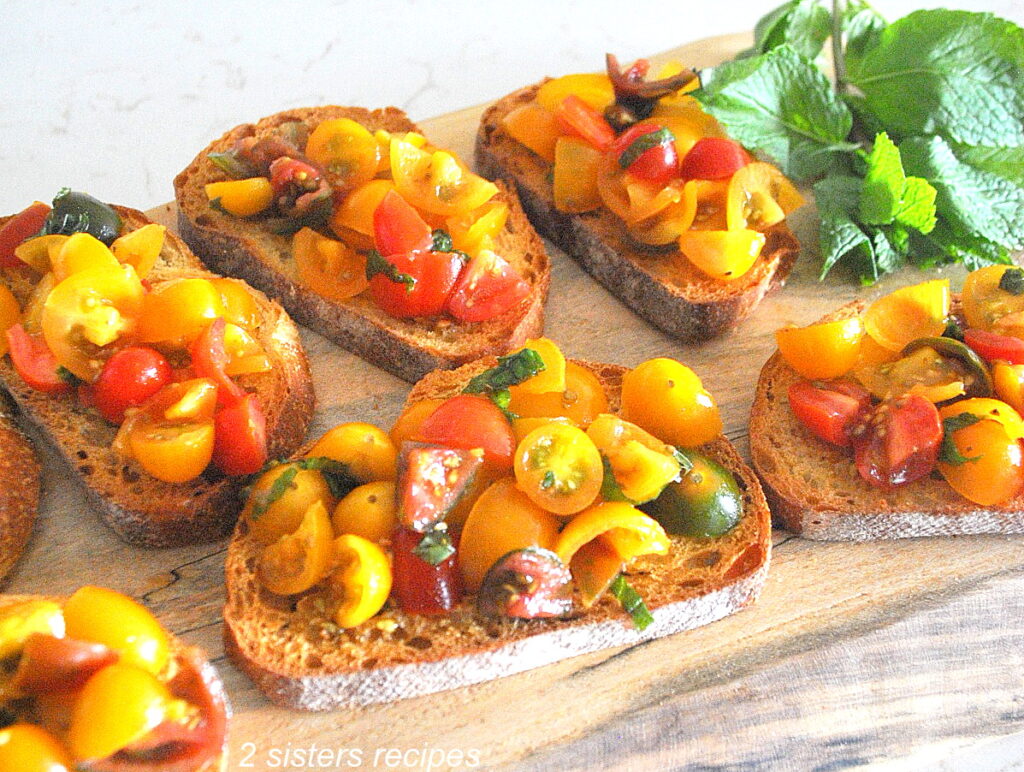 Slices of crusty bread topped with chopped tomatoes and fresh basil served on a wood board.