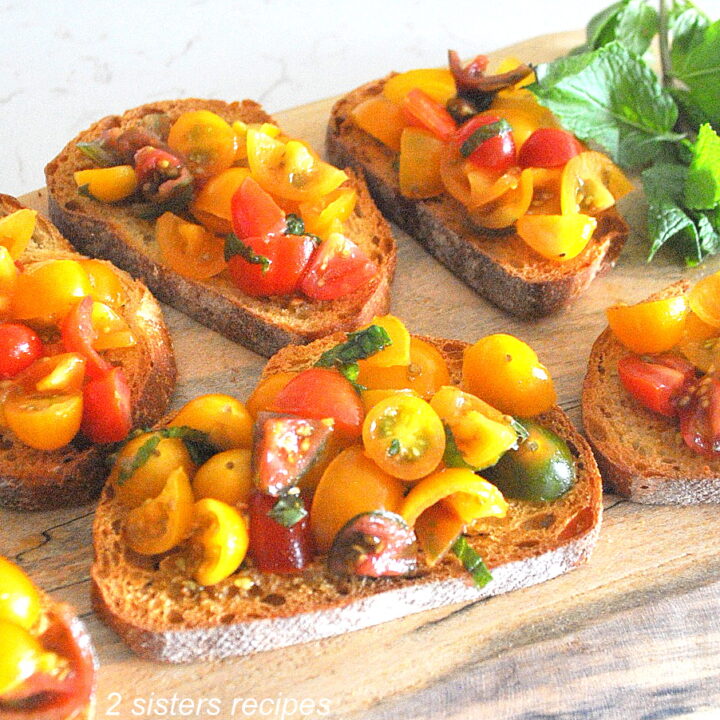 Slices of crusty bread topped with chopped tomatoes and fresh basil served on a wood board.