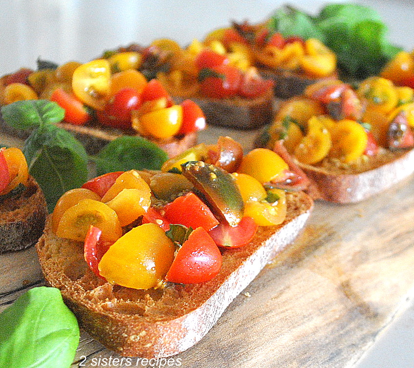 A wooden board filled with crusty breads topped with bruschetta.