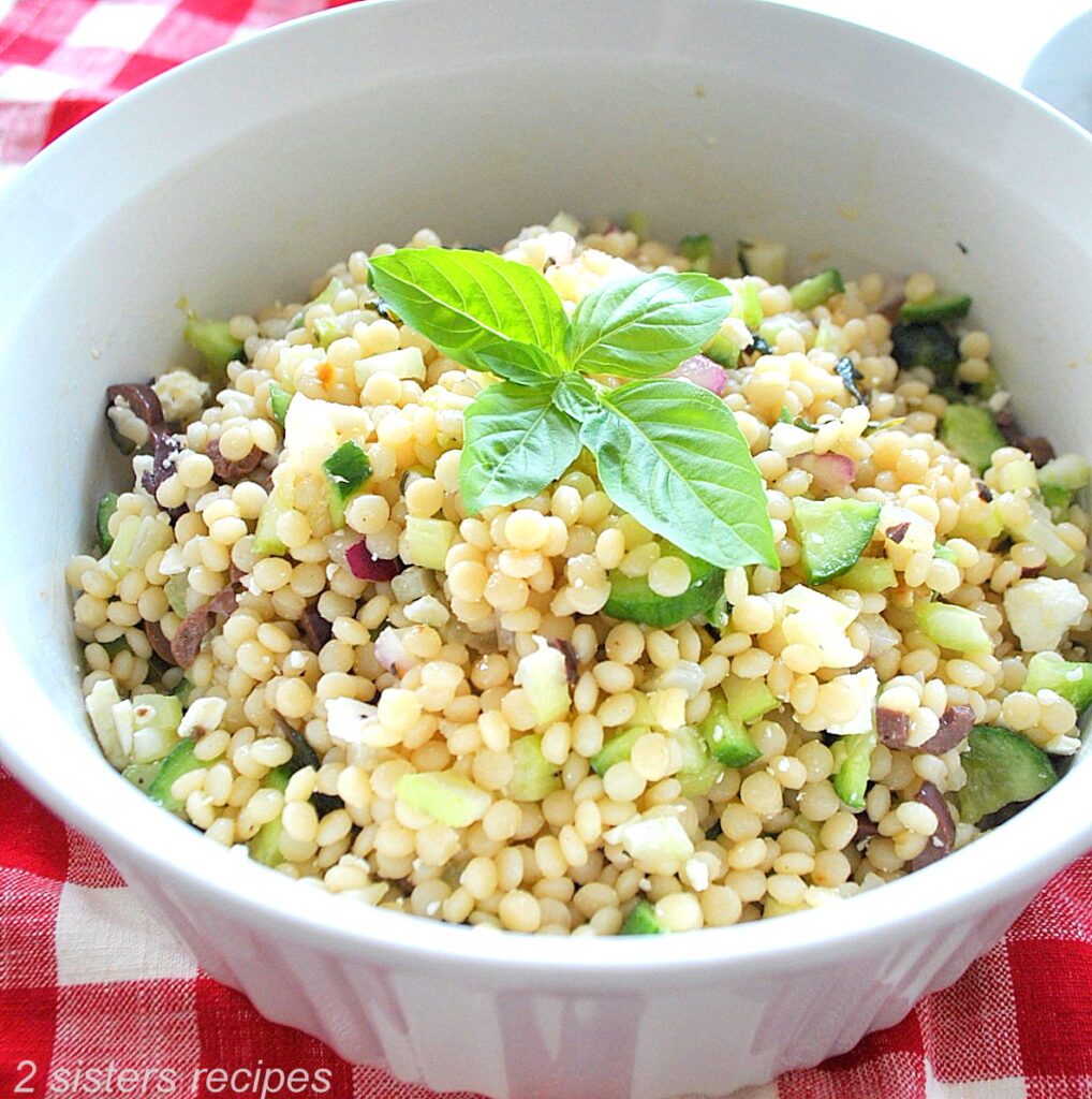 A white bowl filled with pearled couscous salad and a fresh basil leaves on top.