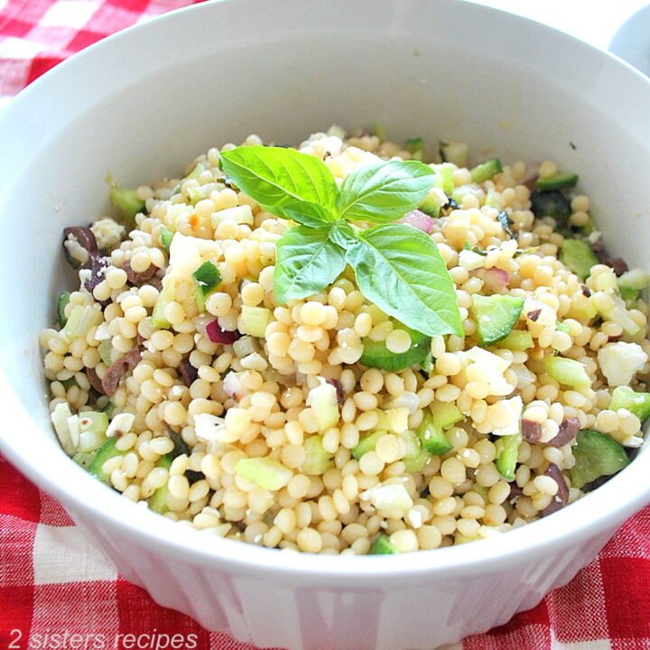 A white bowl filled with pearled couscous salad and a fresh basil leaves on top.