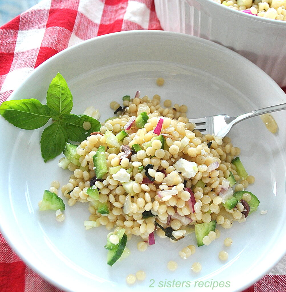 A white dish with a serving of pearled couscous salad and a fork.