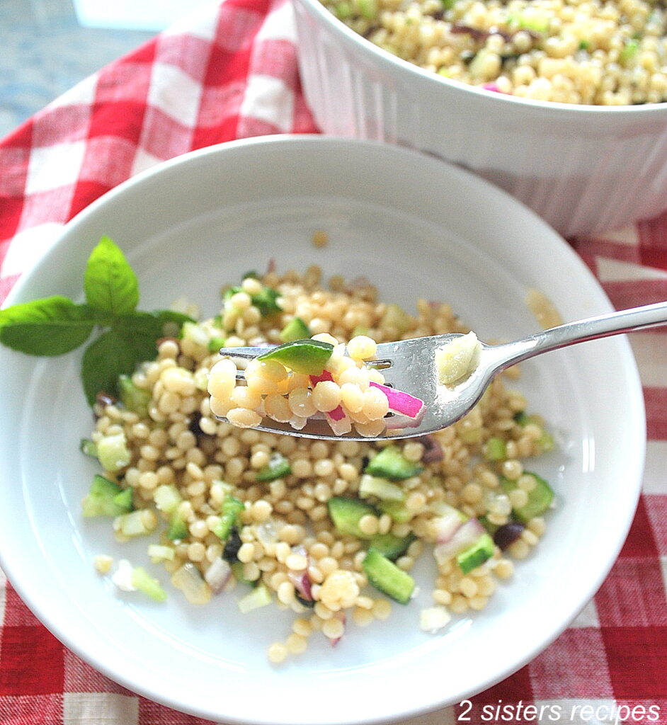 A forkful of white pearled couscous salad in a white plate.