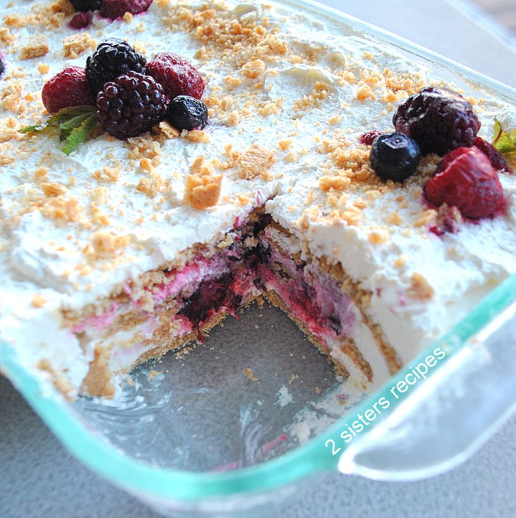 A glass rectangular dish filled with a mixed berry icebox cake with layers of whipped cream inside and on top.