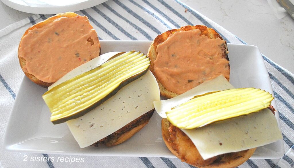 two fish sandwiches with pickles and slice of cheese on top. 