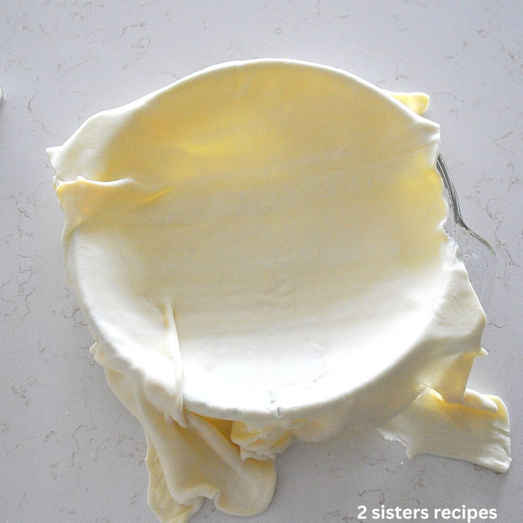 A thawed puff pastry sheet is laid over a glass pie dish. 