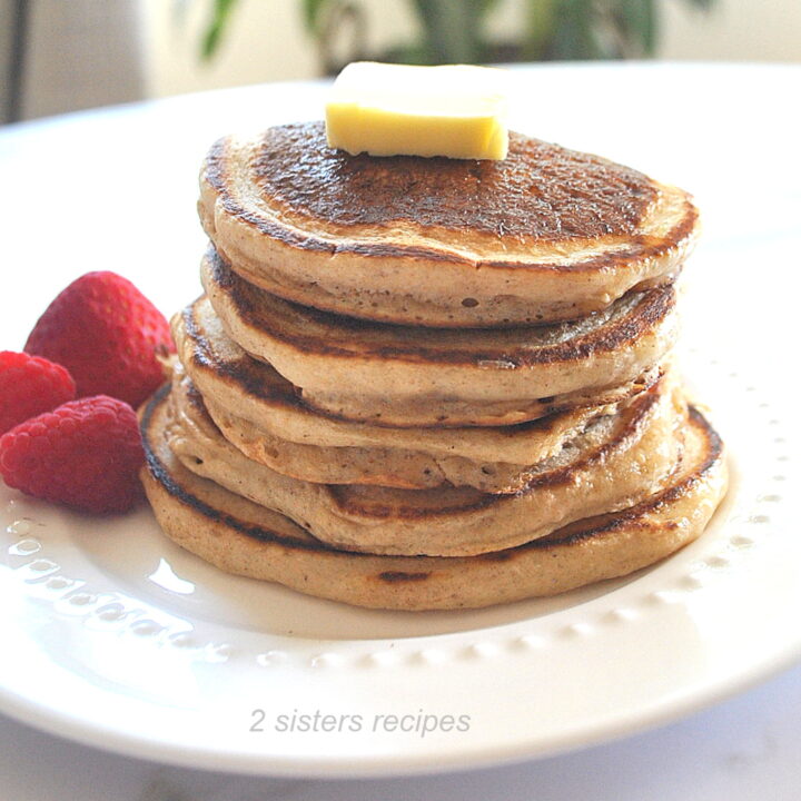 A white plate filled with a pile of eggless pancakes topped with a slice of butter and fresh strawberries on the side.