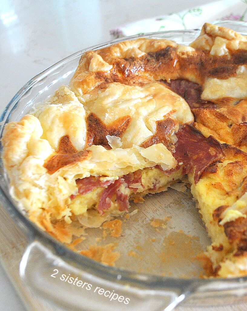 A quiche with salami and cheese  with a piece cut out of it.