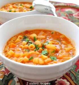 A white bowl of soup in a thick tomato broth with beans and small pasta.