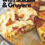 A glass pie dish with a slice of quiche with salami taken out.