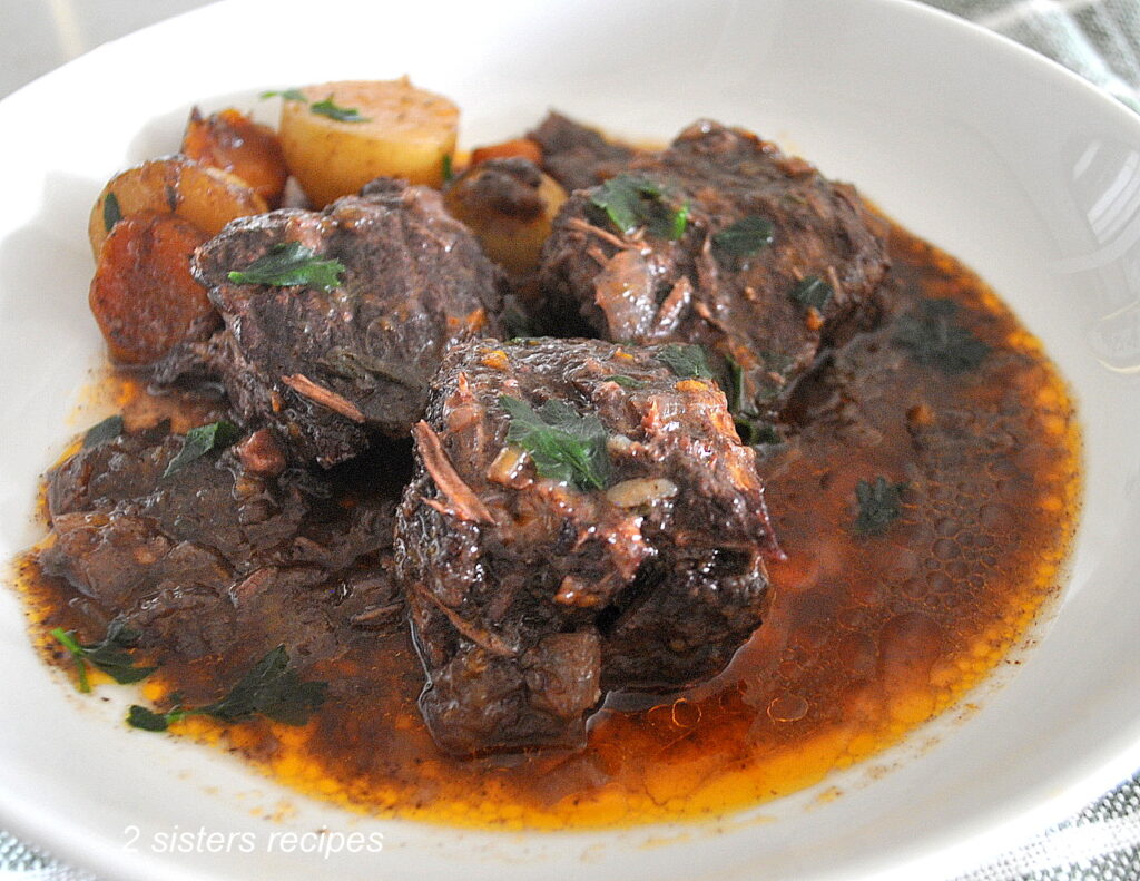 Three boneless short ribs with sauce served in a white plate with some veggies.