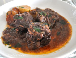 Three boneless short ribs with sauce served in a white plate with some veggies.