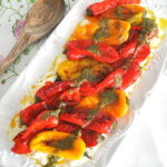 A white platter will charred mini peppers over creamy ricotta, topped with a drizzle of pesto sauce.