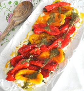 A white platter will charred mini peppers over creamy ricotta, topped with a drizzle of pesto sauce.