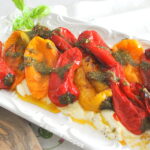 A white platter with a bed of ricotta with charred peppers.