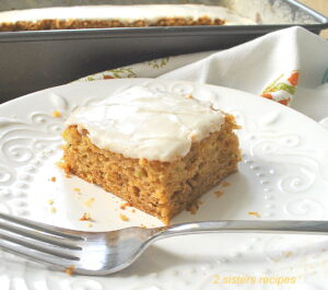 A slice of zucchini lemon snack cake topped with icing and served on a white plate with a fork.