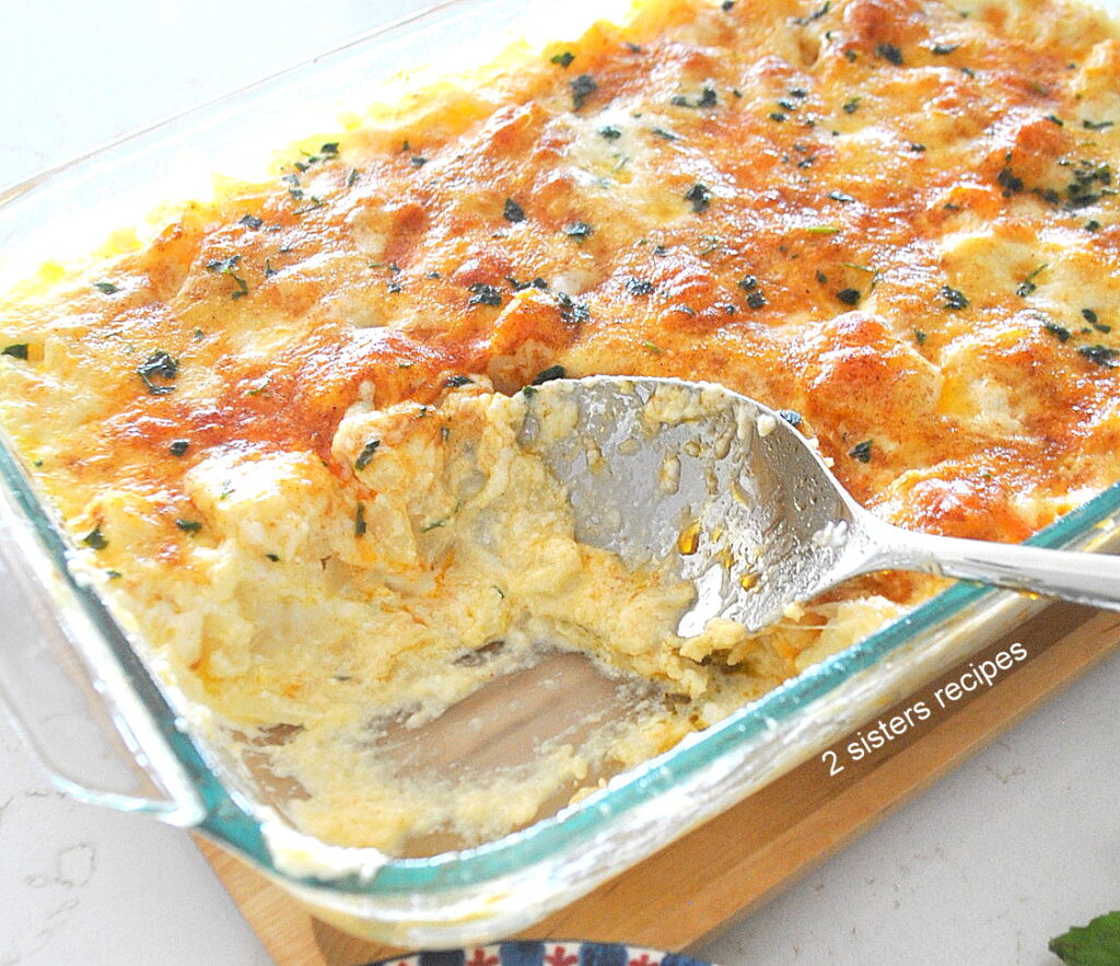 A glass baking dish filled with a creamy potato and cheese casserole and with a spoon inside.