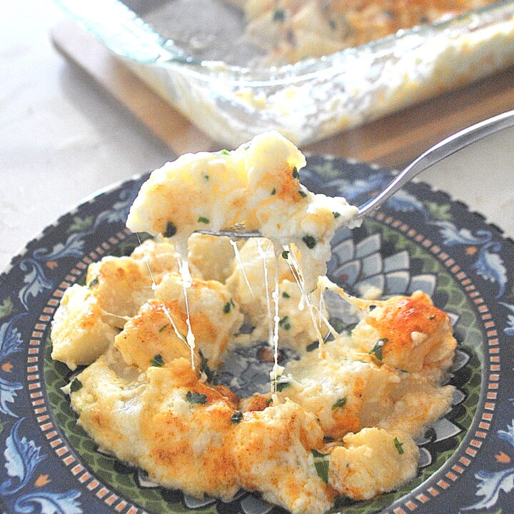 A forkful of cheesy potato casserole served on a blue colorful plate.