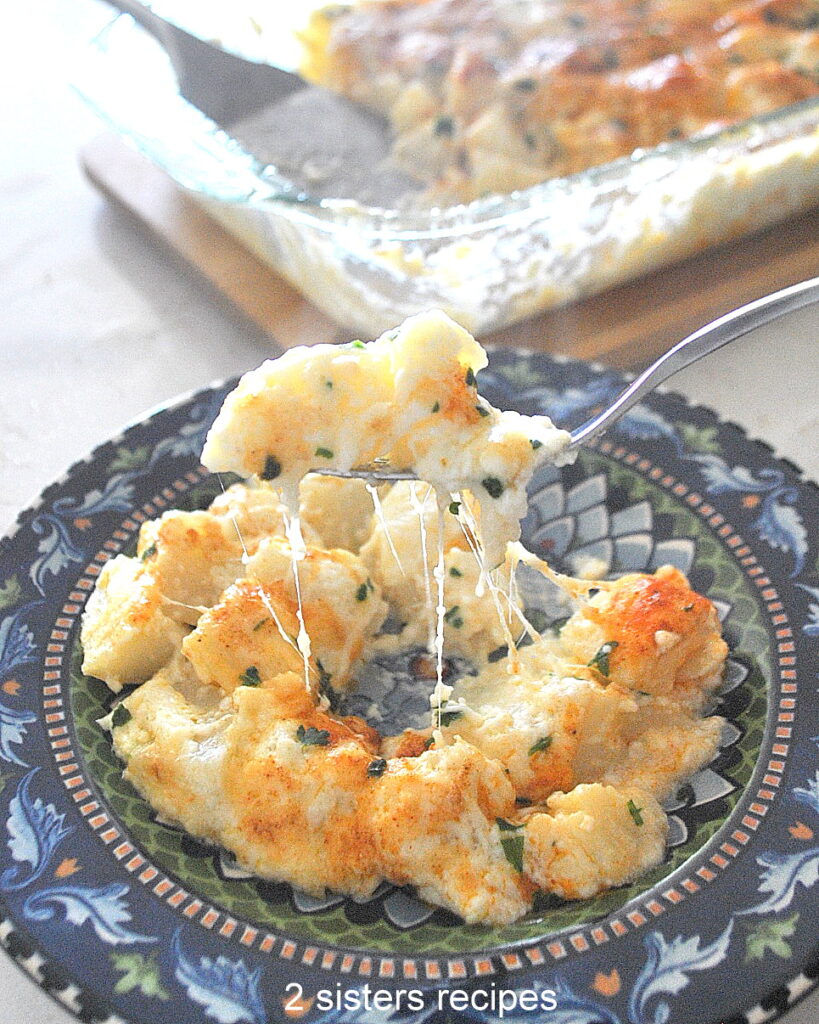 A forkful of cheesy potato casserole served on a blue colorful plate.