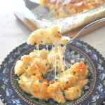 A forkful of cheesy potato casserole served on a blue colorful plate.