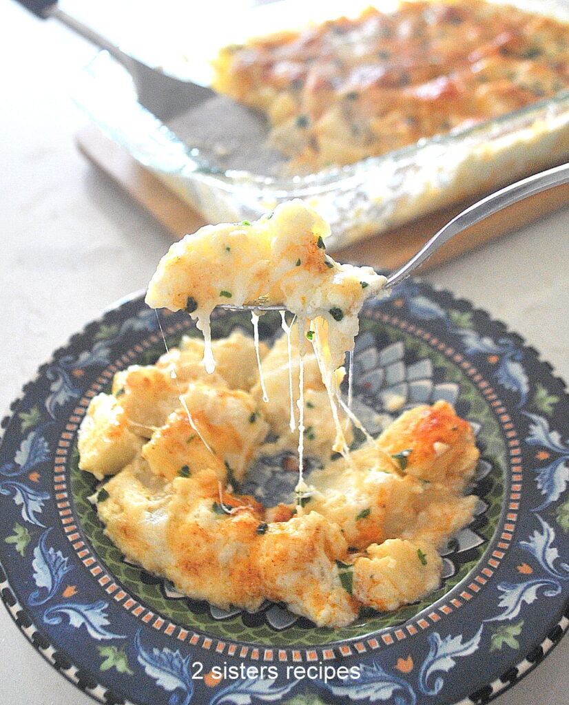 A forkful of cheesy potato casserole served on a blue colorful plate.