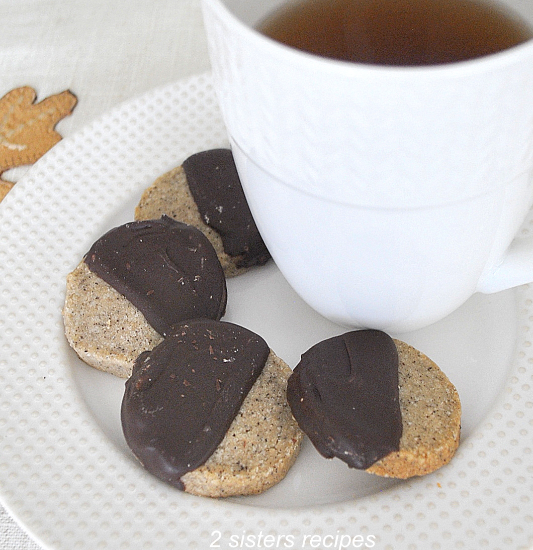 A white plate and coffee mug with 4 espresso shortbread cookies dipped in chocolate.