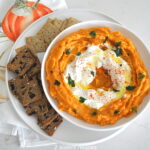 White bowl filled with sweet potato dip with white cream in the center and crackers surrounding the bowl.