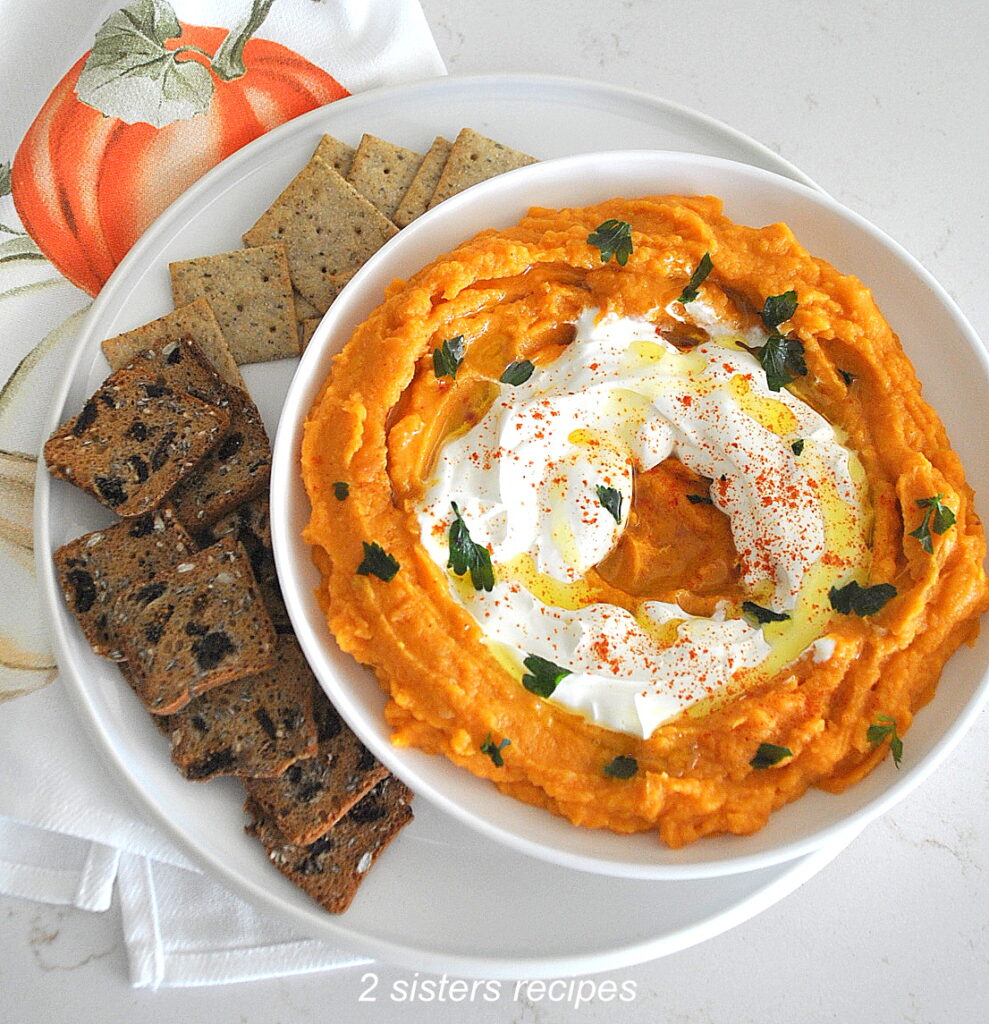 White bowl filled with sweet potato dip with white cream in the center and crackers surrounding the bowl.