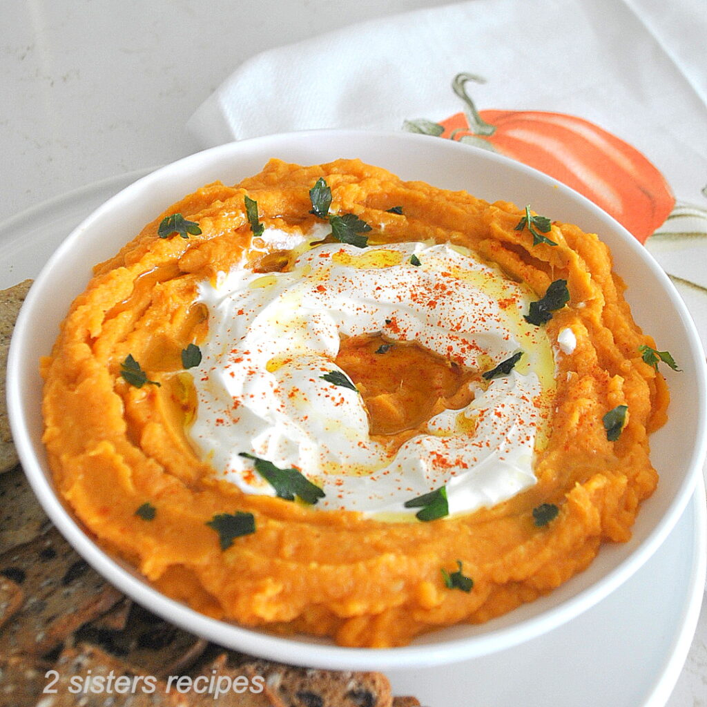 A white dish filled with sweet potato dip with white cream in the center.