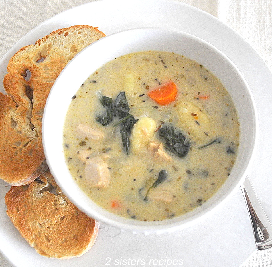 A white bowl filled with a creamy chicken gnocchi soup with veggies and toast on the side.