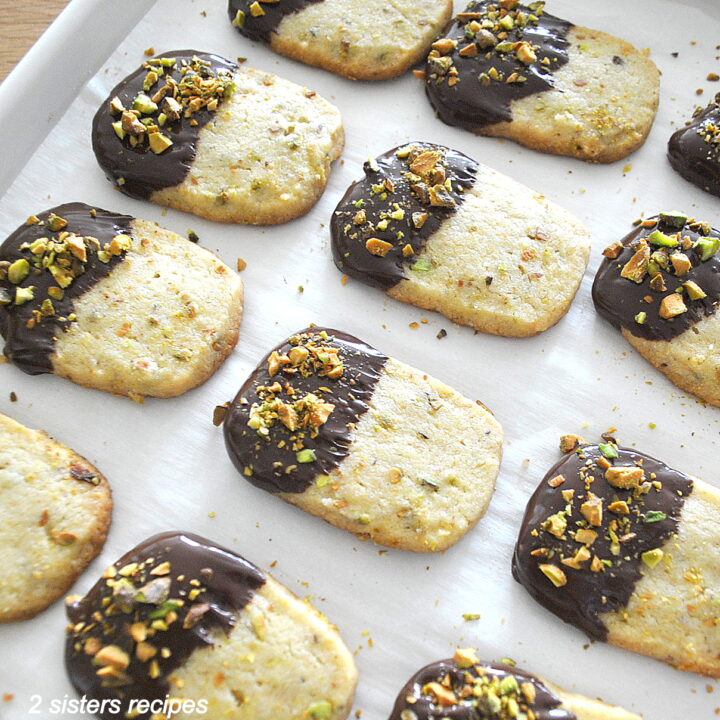 A baking sheet filled with chocolate-dipped pistachio shortbread cookies.