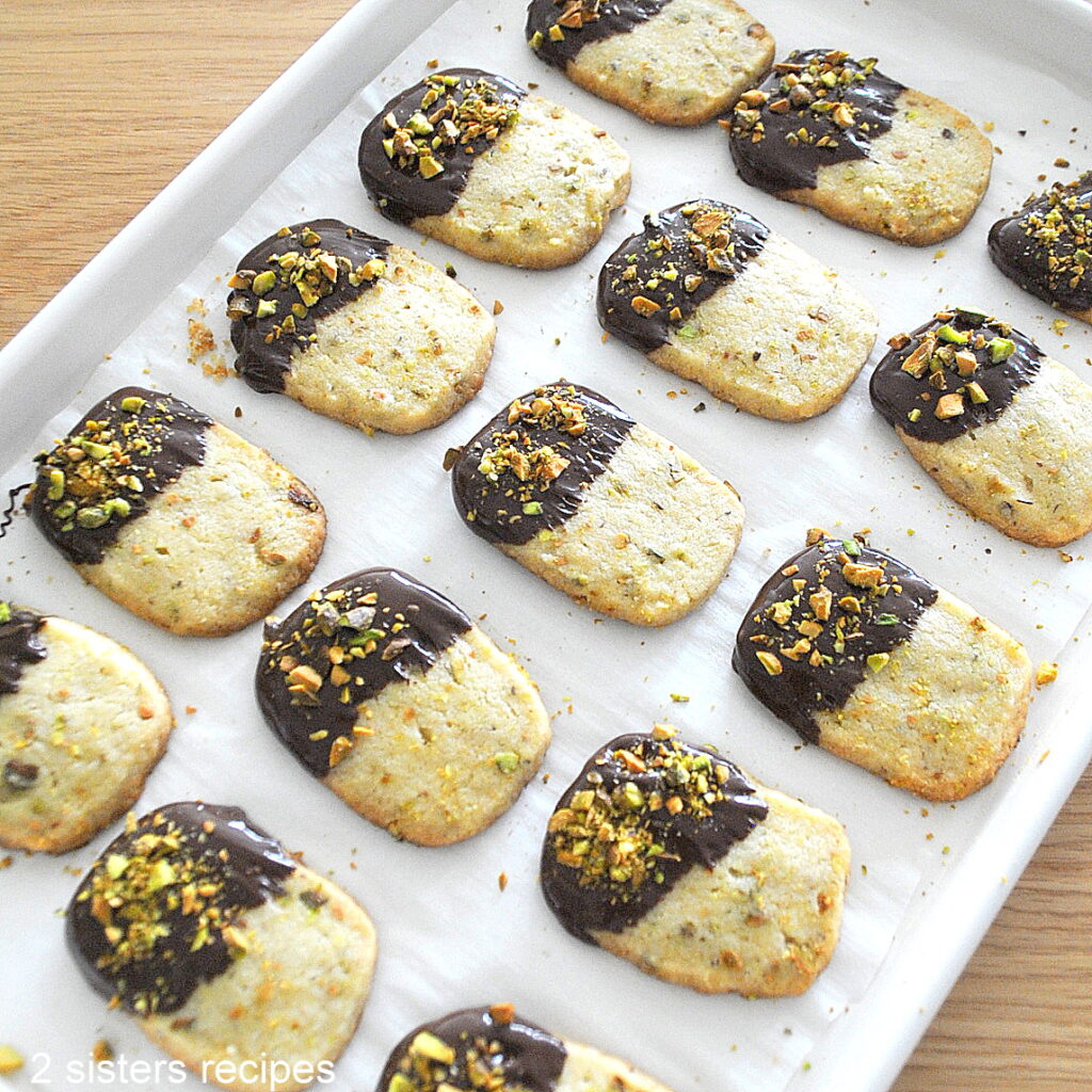 A baking sheet filled with chocolate-dipped pistachio shortbread cookies.