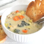 A white bowl filled with chicken gnocchi soup with veggies and a slice of toast dunk into the souo.
