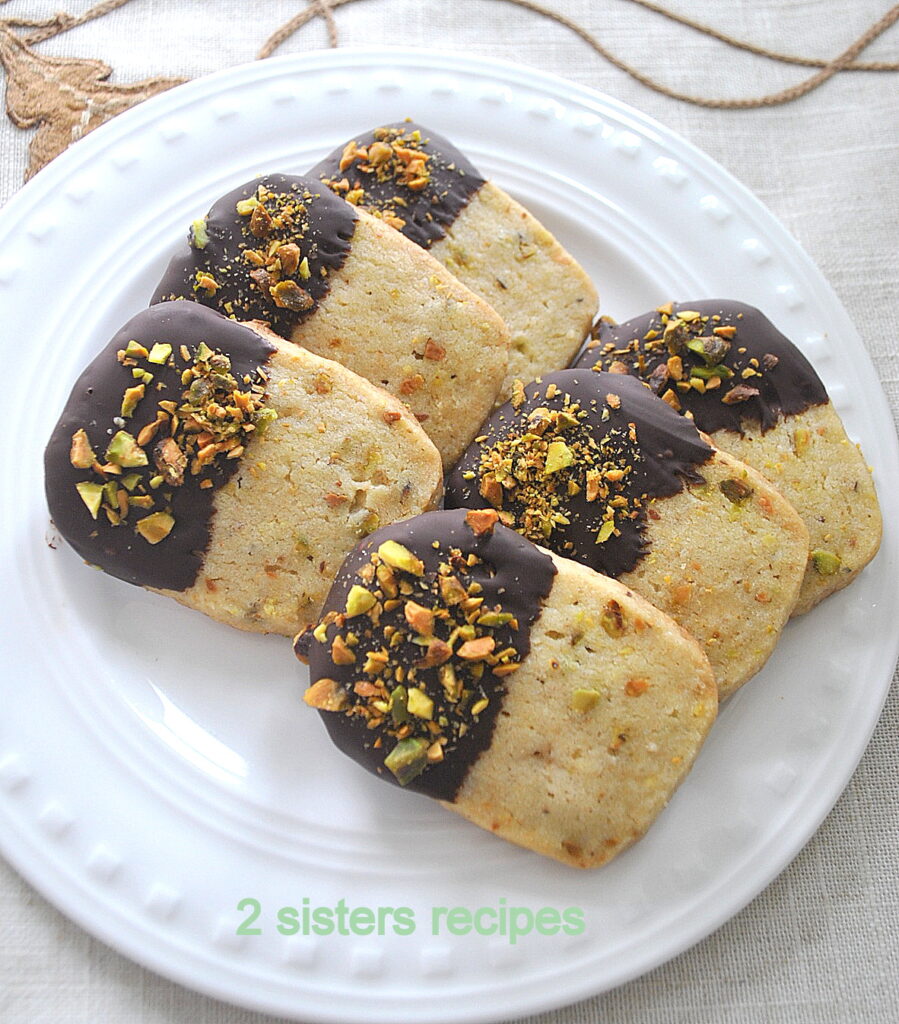 A white plate with chocolate dipped cookies with crushed pistachios on top.