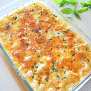 A pyrex glass baking dish filled with a baked potato and Gruyere cheese, casserole. topped with smoked paprika.