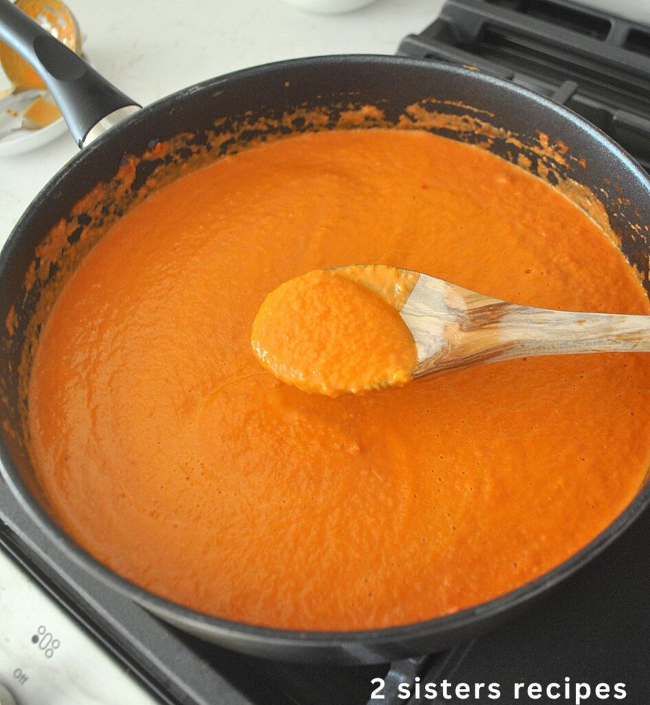 A black skillet on stove top with orange-color Vodka sauce and a wooden spoon.