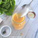 A mason jar filled with a salad dressing and a spoonful .