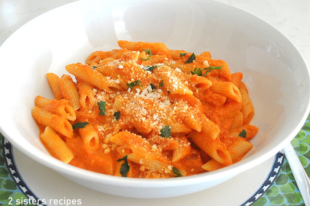 A white bowl filled with penne with Vodka sauce, some grated cheese on top.