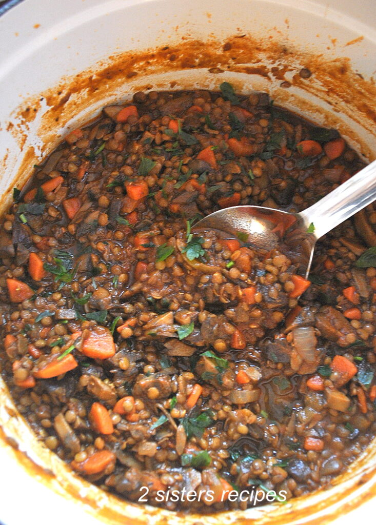 A Dutch oven pot filled with mushrooms, lentils and carrots with a large spoon inside.
