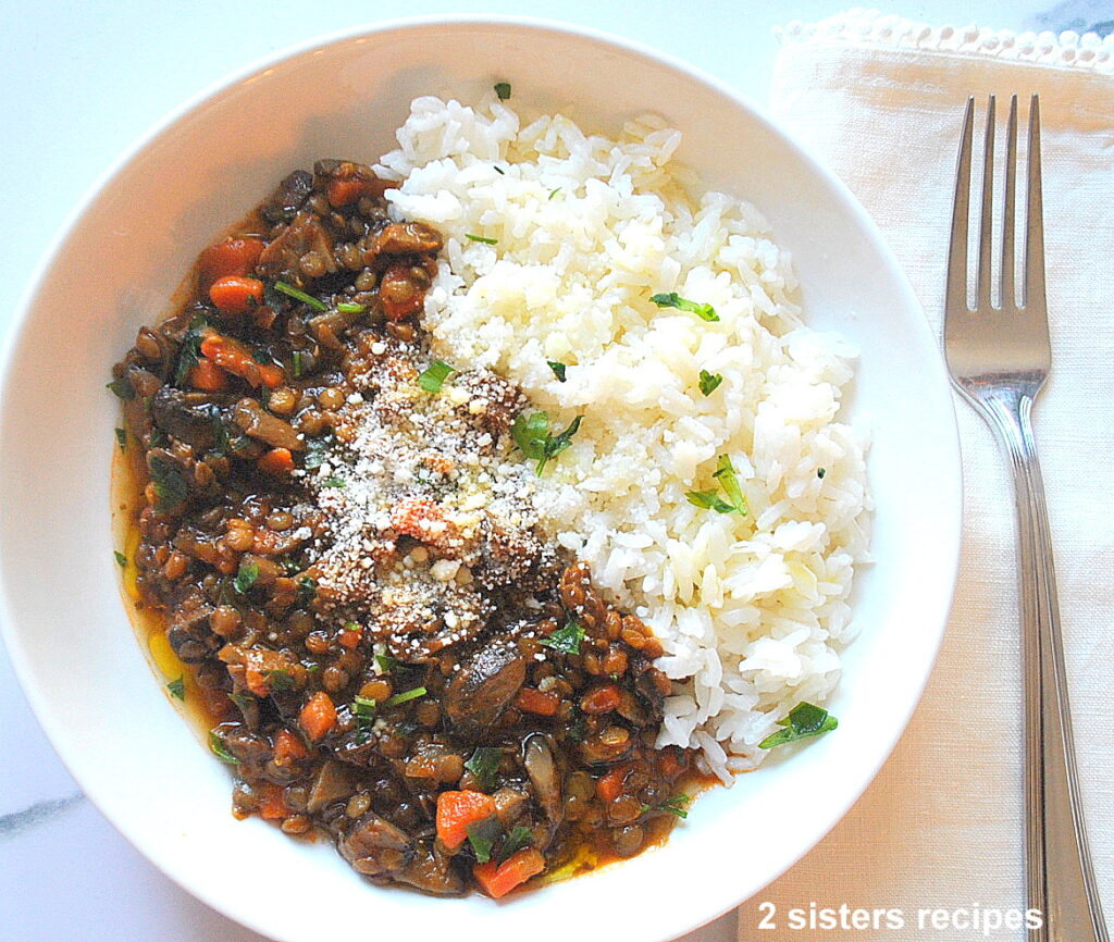 A white bowl filled with a mushroom and lentil stew with a side of white rice and some grated parmesan cheese on top.