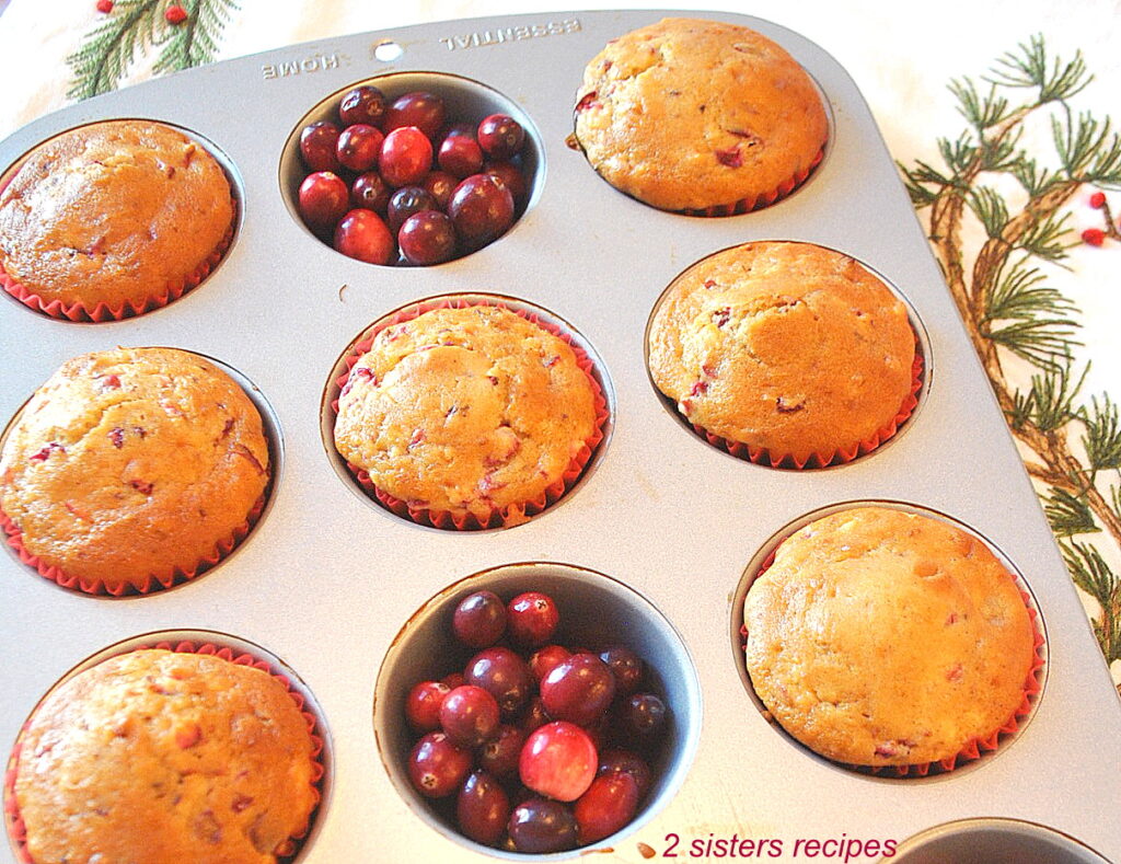 A muffin pan filled with baked muffins and fresh cranberries .