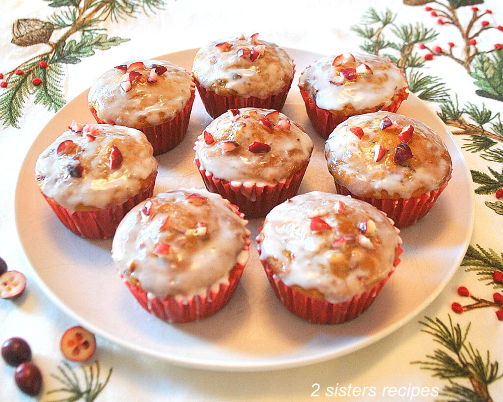 A white plate filled with baked cranberry orange muffins topped with a glaze.