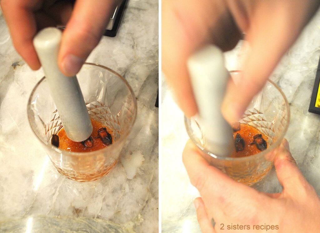 A cocktail glass with a muddler the ingredients in the glass.