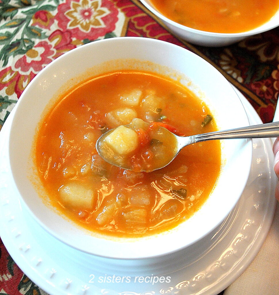 A white bowl loaded with chunks of chopped potatoes in a tomato broth. 