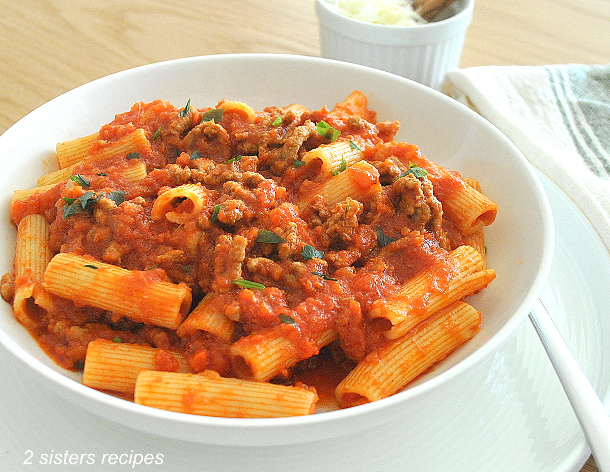 A white plate filled with rigatoni pasta topped with lamb bolognese sauce.