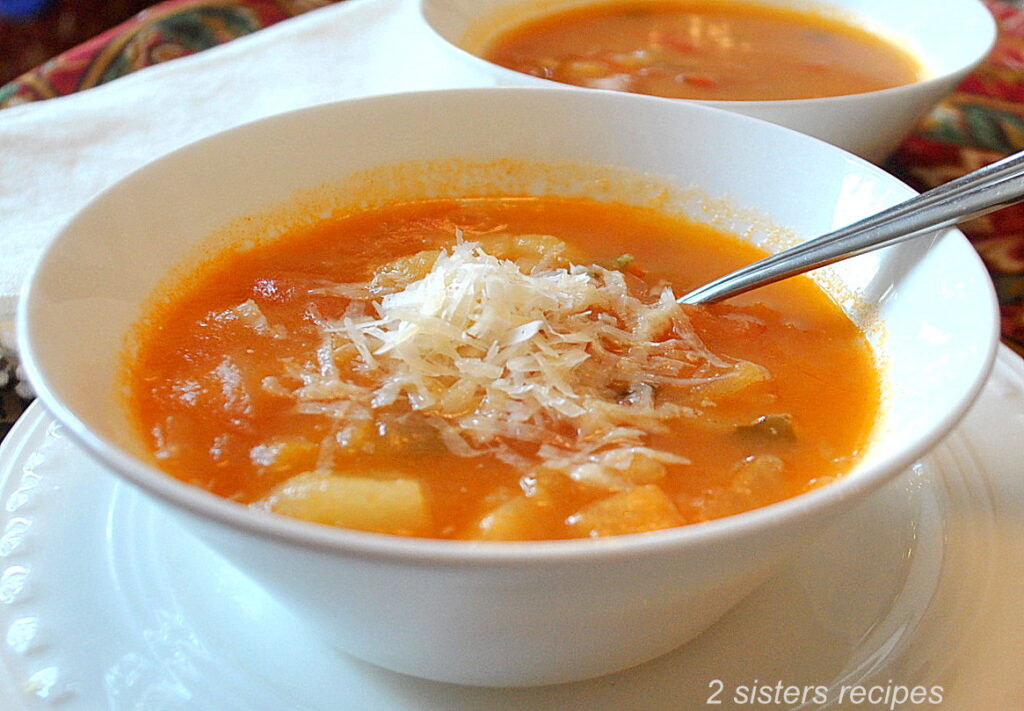 A bowl of soup with grated cheese on top and a spoon inside.