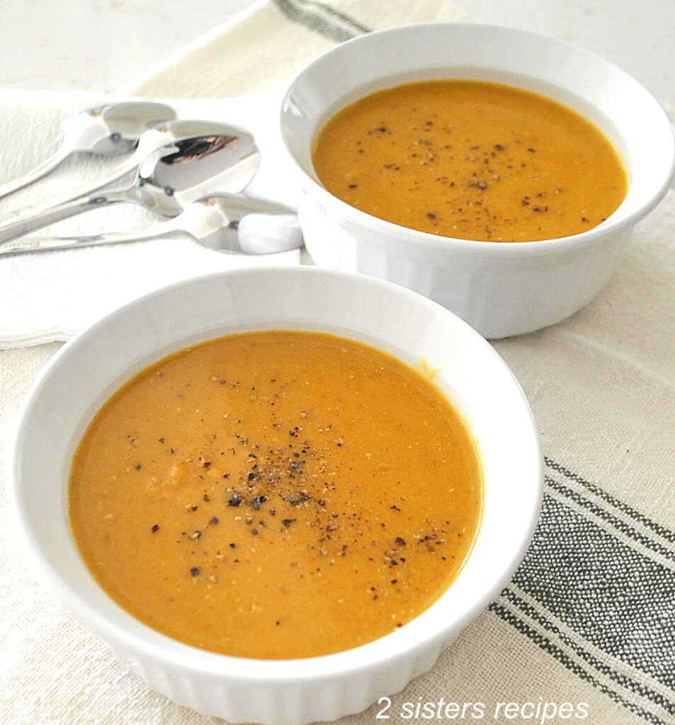 Two white bowls of creamy butternut squash & red lentil soup with black pepper on top.