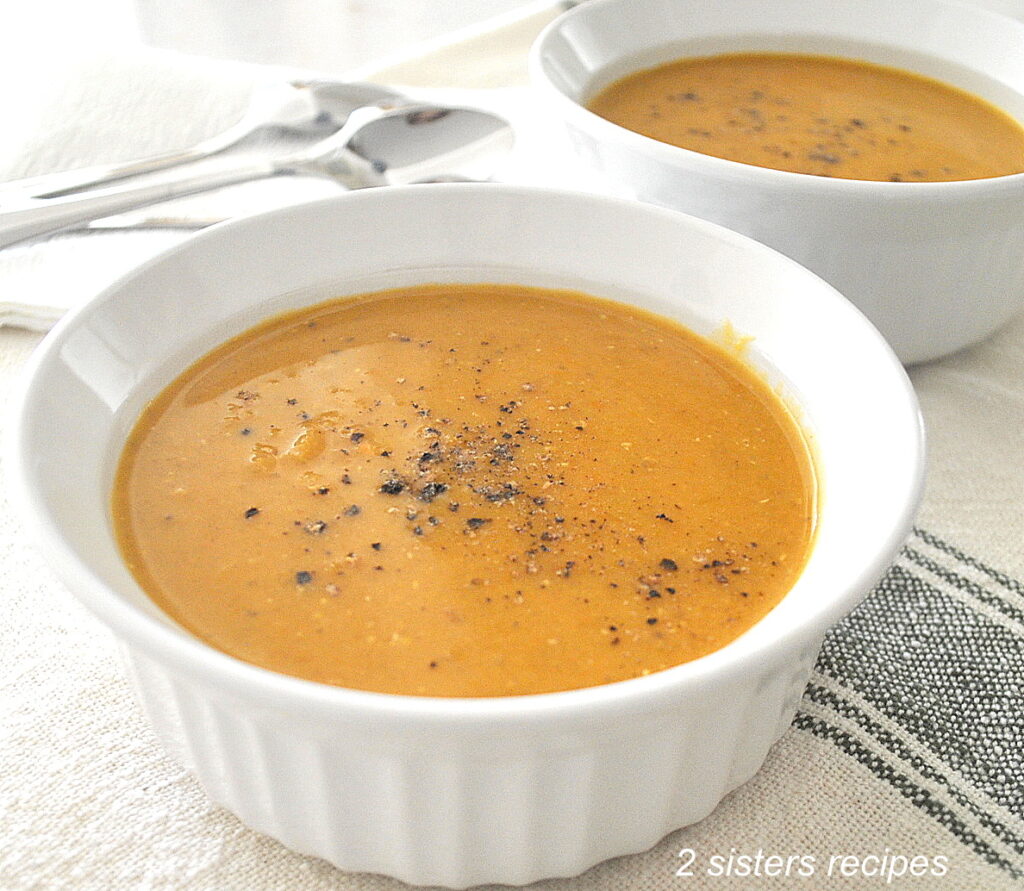 Two white bowls filled with a creamy orange-colored soup topped with cracked black pepper.
