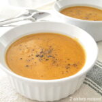 Two white bowls filled with a creamy orange-colored soup topped with cracked black pepper.