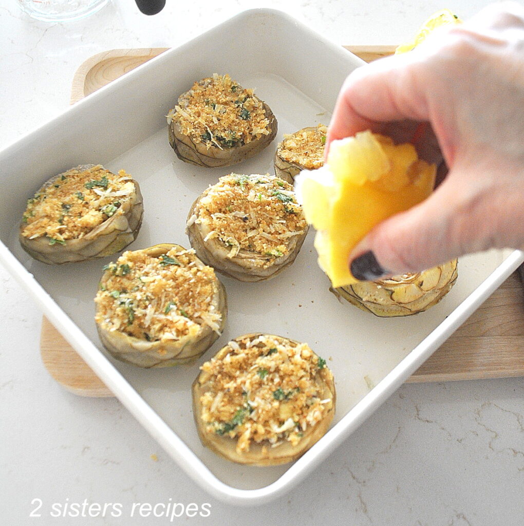 Squeezing a lemon into the water of the stuffed artichoke bottoms.